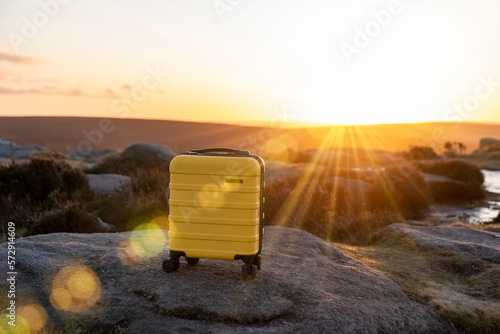 Yellow Suitcase  on top of hill or mountain against blue sky at sunrise. Travel concept. photo