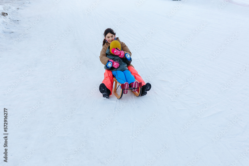 two girls sledding on snow slope at wooden sleigh