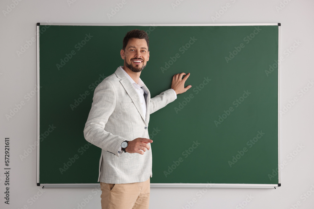 Happy teacher explaining something at blackboard in classroom. Space for text Happy teacher explaining something at blackboard in classroom. Space for text