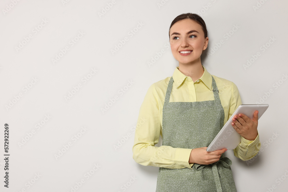 Beautiful young woman in clean apron with tablet on light grey background. Space for text Beautiful young woman in clean apron with tablet on light grey background. Space for text