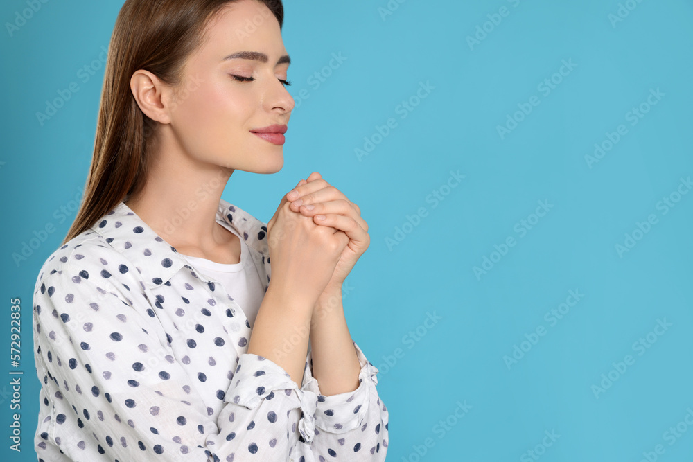 Woman with clasped hands praying on turquoise background, space for text
