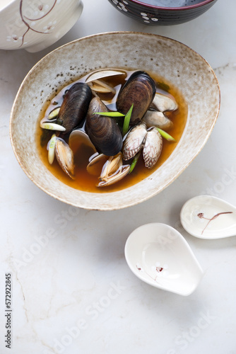 Asian style miso soup with littleneck clams and mussels, elevated view on a light-beige marble background, vertical shot with space photo