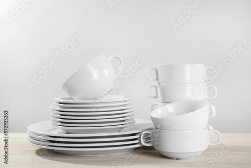 Set of clean dishware on white wooden table against light background