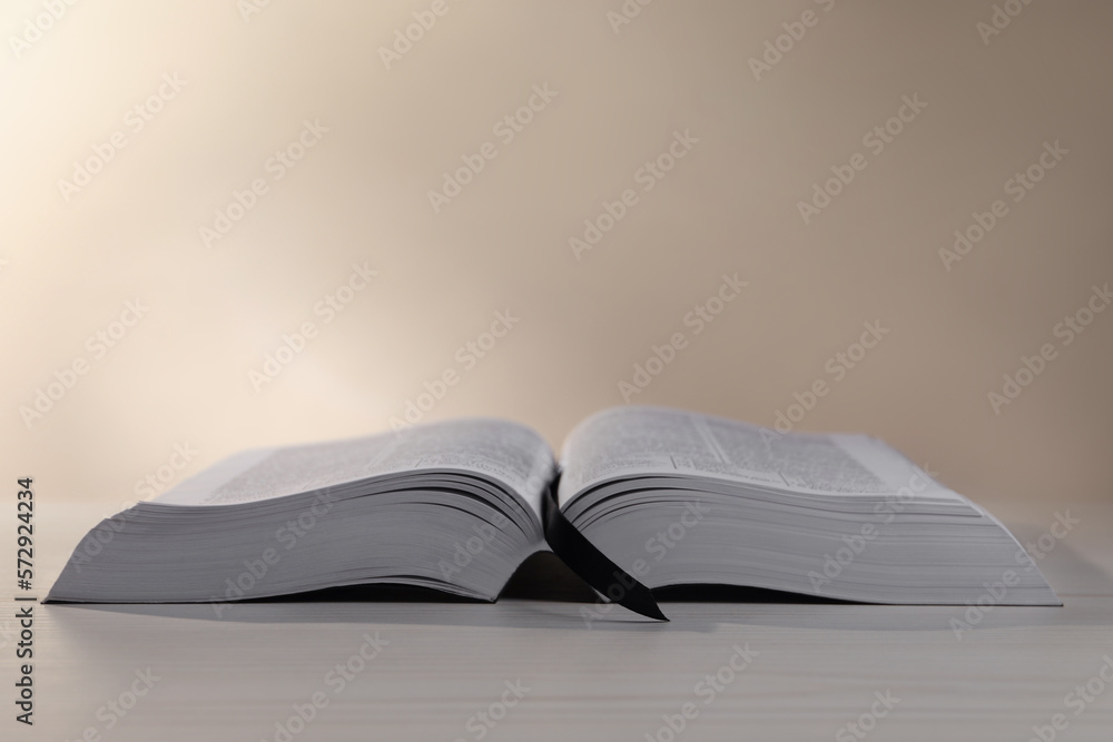 Naklejka premium Open Bible on white wooden table against beige background. Space for text