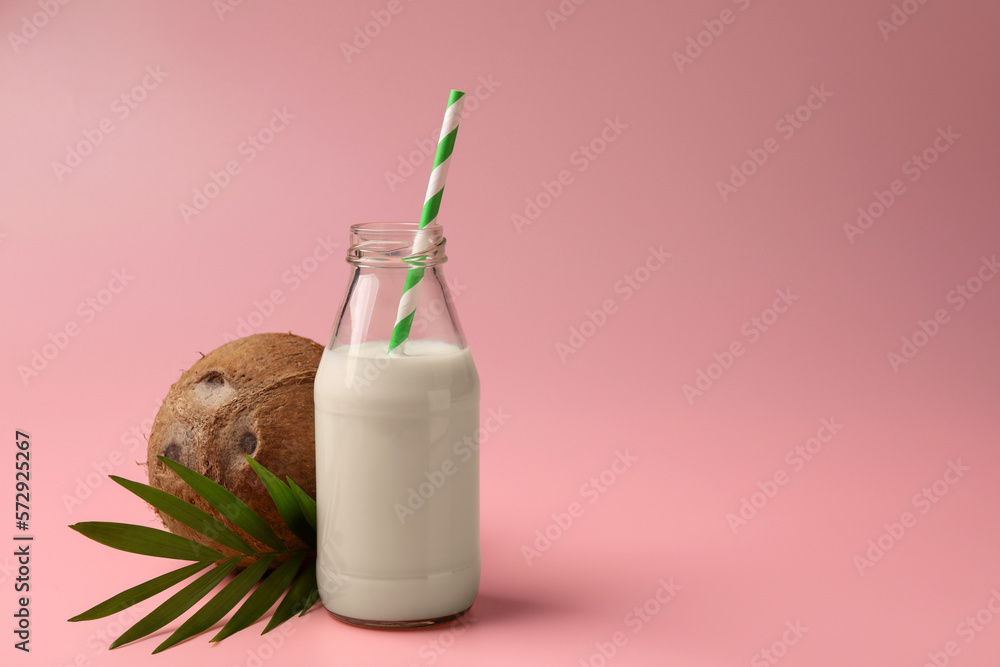 Glass bottle of delicious vegan milk, coconut and leaf on pink background, space for text Glass bottle of delicious vegan milk, coconut and leaf on pink background, space for text