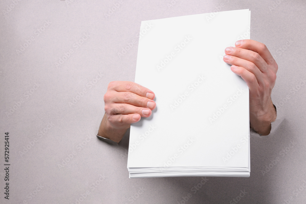 Man holding sheets of paper through holes in white paper, closeup. Mockup for design Man holding sheets of paper through holes in white paper, closeup. Mockup for design