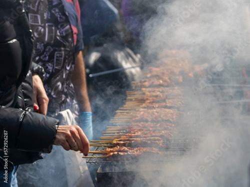 Wooden meat skewers on barbecue grill with smoke and hands at Tsiknopempti (Smokey Thursday), Limassol, Cyprus