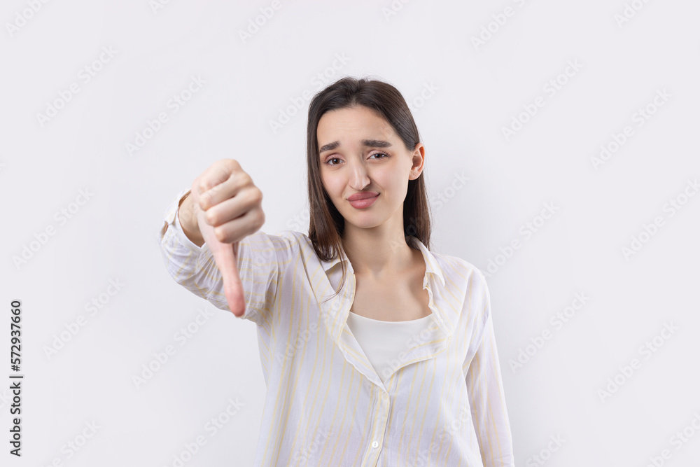 Young brunette in a blue tank top giving thumb down gesture looking with negative expression Young brunette in a blue tank top giving thumb down gesture looking with negative expression