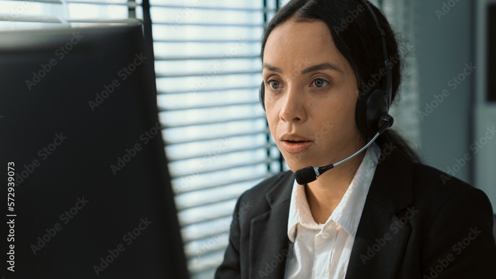 Competent female operator working on computer and talking with clients ...