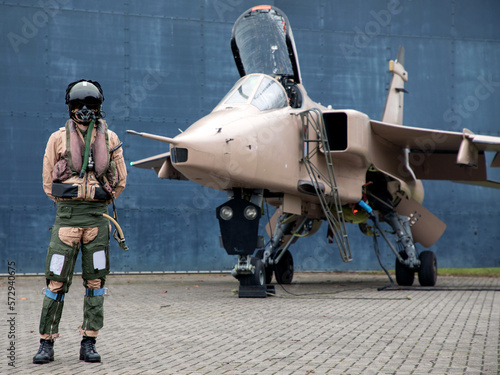 Fotografija Fighter pilot standing with Military fighter Jet wearing flying helmet, suit and