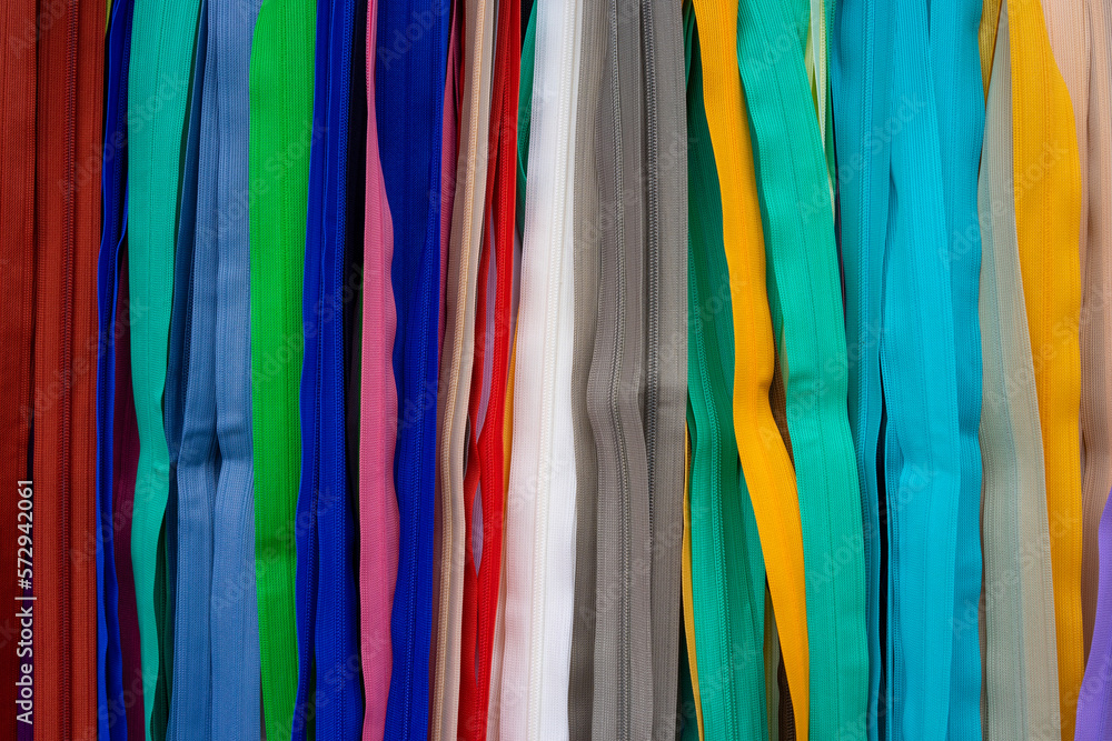 Many colorful zippers hang vertically next to each other from top to bottom in a tailor's shop. Different colors in a row next to each other