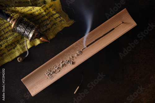 Overhead view of burning incense stick on wooden incense holder and tibetan hand prayer wheel on prayer flag