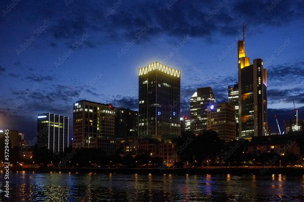 Stimmungsvoll beleuchtete Frankfurter Skyline bei Nacht mit blauem Himmel und dunklen Wolken