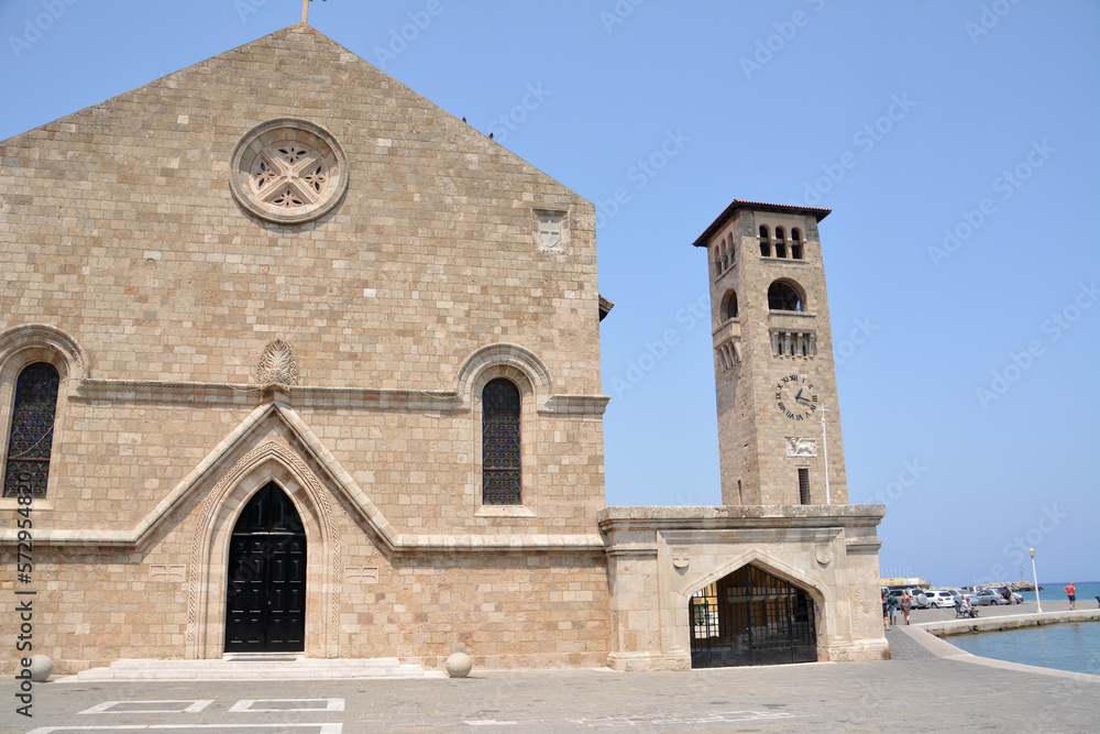 medieval cathedral with tower clock, arched windows and doors and stone square on Rhodes island