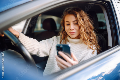Young woman sitting in a car in the driver\'s seat looking into a smartphone, paying for parking and navigating in the city