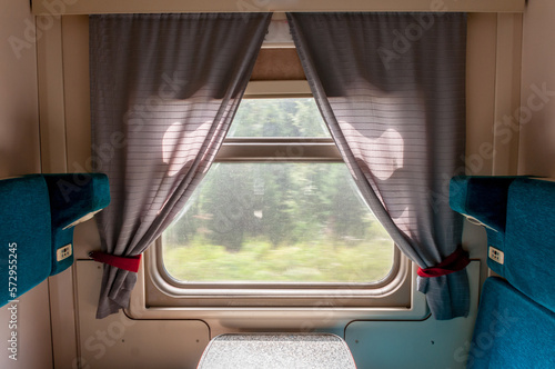 A window and part of the interior of a compartment car inside a traveling train in summer