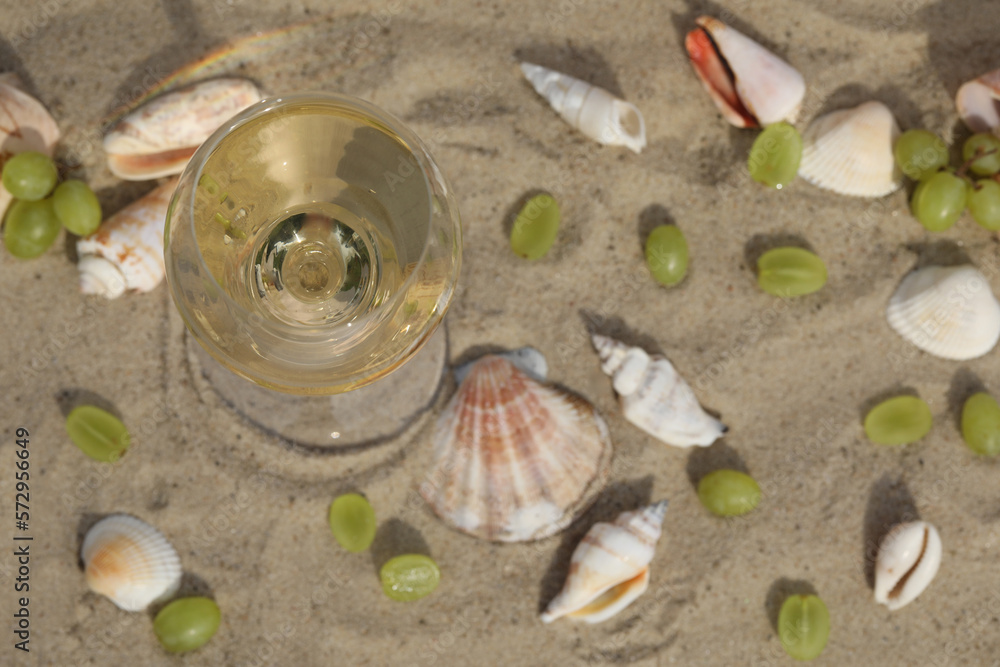 glass of white wine on sand as background with shells