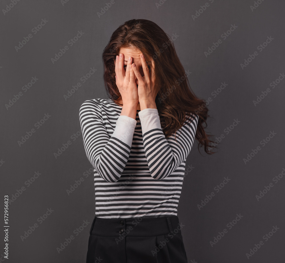 Beautiful young business tired woman hiding and covering the face the palms of hands on grey background. Closeup. Beautiful young business tired woman hiding and covering the face the palms of hands on grey background. Closeup.