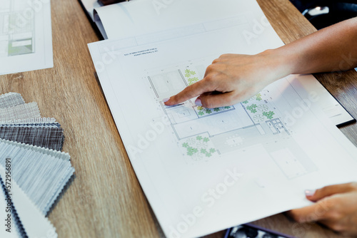 Close-up of an Architect pointing with her finger at a blueprint. She is analyzing the architectural project of a house while working in her office. Young professional concept.