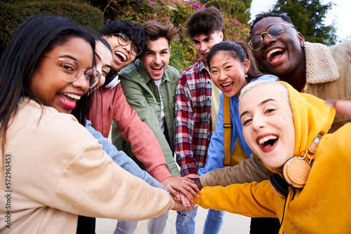 Fotografía Cheerful multiracial group of students making pile hands and smiling at the camera on campus