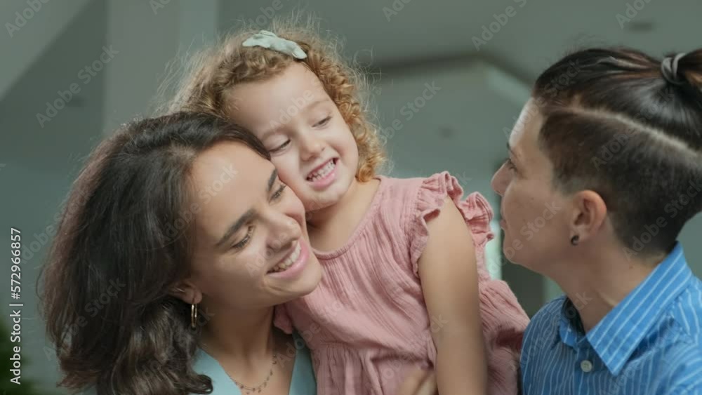 Pretty 2 year old girl with beautiful curly fair hair and blue eyes playing with her moms at home being kissed and hugged by them with tenderness and love Pretty 2 year old girl with beautiful curly fair hair and blue eyes playing with her moms at home being kissed and hugged by them with tenderness and love