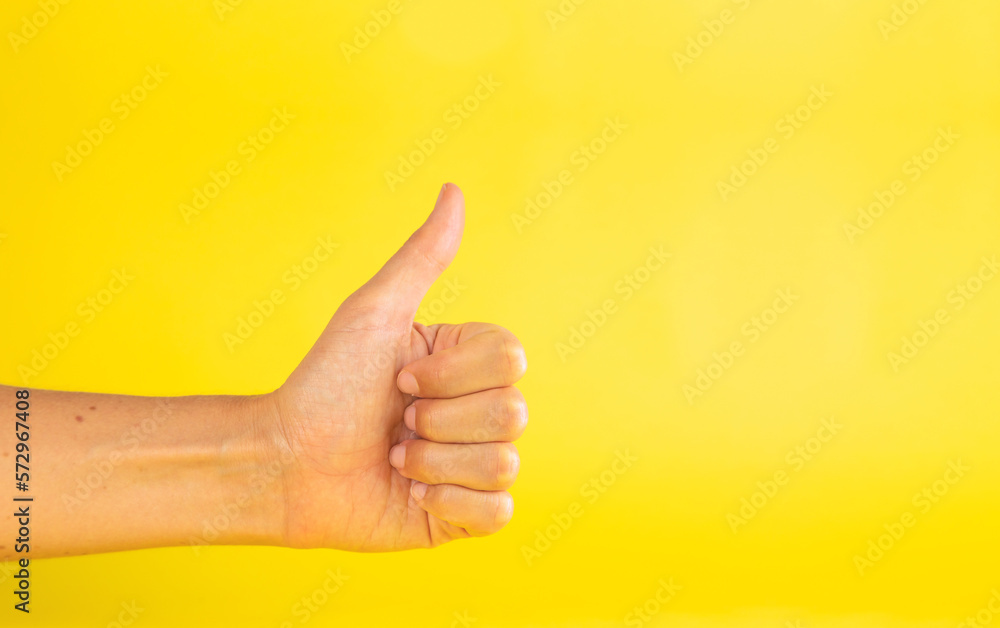 A woman's hand, with thumb up finger, making a gesture of like, or ok, on a yellow background