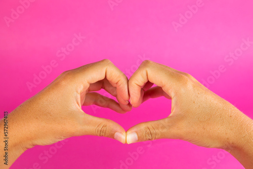 A woman s hands forming a love heart with fingers  on a fuchsia pink background