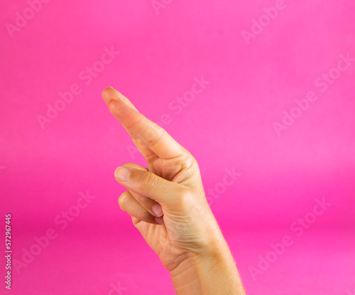 A woman's hand, fingers crossed, wishing luck, on a plain fuchsia pink background