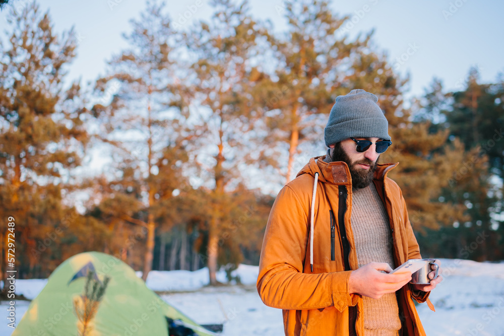 After the ascent, the tourist admires the sunset while standing near the tent with a cup of tea or coffee and takes a photo on his phone. After the ascent, the tourist admires the sunset while standing near the tent with a cup of tea or coffee and takes a photo on his phone.