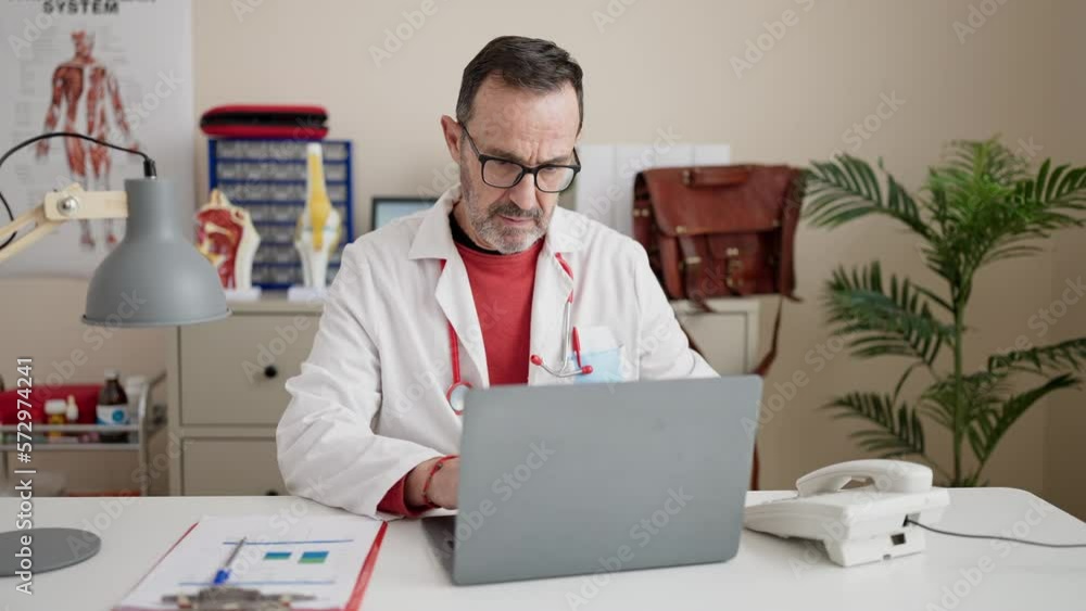 Middle age man doctor using laptop working at clinic Middle age man doctor using laptop working at clinic