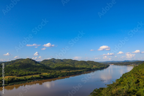 Beautiful natural scenery of river in tropical green forest with trees on two sides and mountain in background