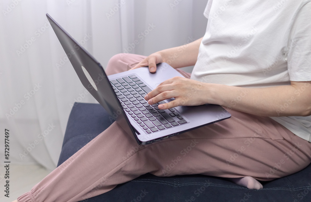 Naklejka premium Pregnant woman in white clothes sitting and using laptop in sofa. Baby expectation. Homely atmosphere.