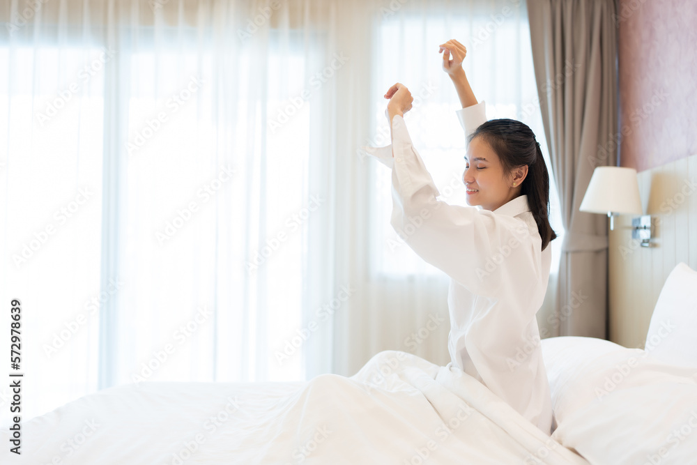 Asian women wake up in the morning In the bedroom of the house, the surrounding environment resembled a hotel. She smiled with freshness and relief. have good health wearing long-sleeved white pajamas Asian women wake up in the morning In the bedroom of the house, the surrounding environment resembled a hotel. She smiled with freshness and relief. have good health wearing long-sleeved white pajamas