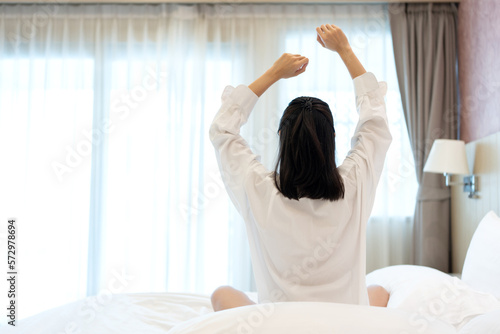 portrait of asian woman back In the bedroom of a house similar to a hotel She has long hair and wears white pajamas. Wake up refreshed and relaxed. Hands up. Pillow and blanket available