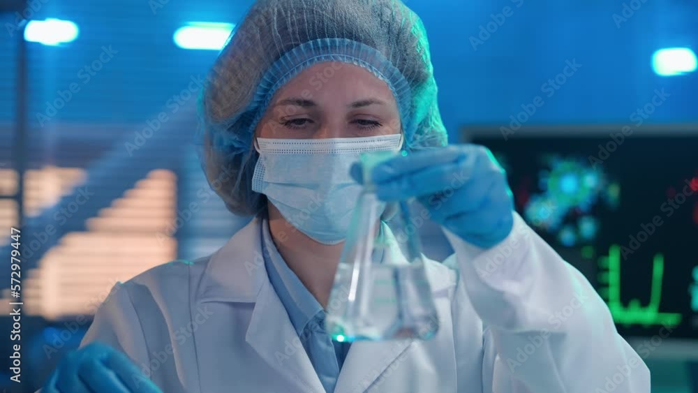 A female scientist adds brown powder to a clear liquid in a flask. The woman observes the reaction of the sample and stirs the liquid. Research in a modern biochemical laboratory. Close up. A female scientist adds brown powder to a clear liquid in a flask. The woman observes the reaction of the sample and stirs the liquid. Research in a modern biochemical laboratory. Close up.