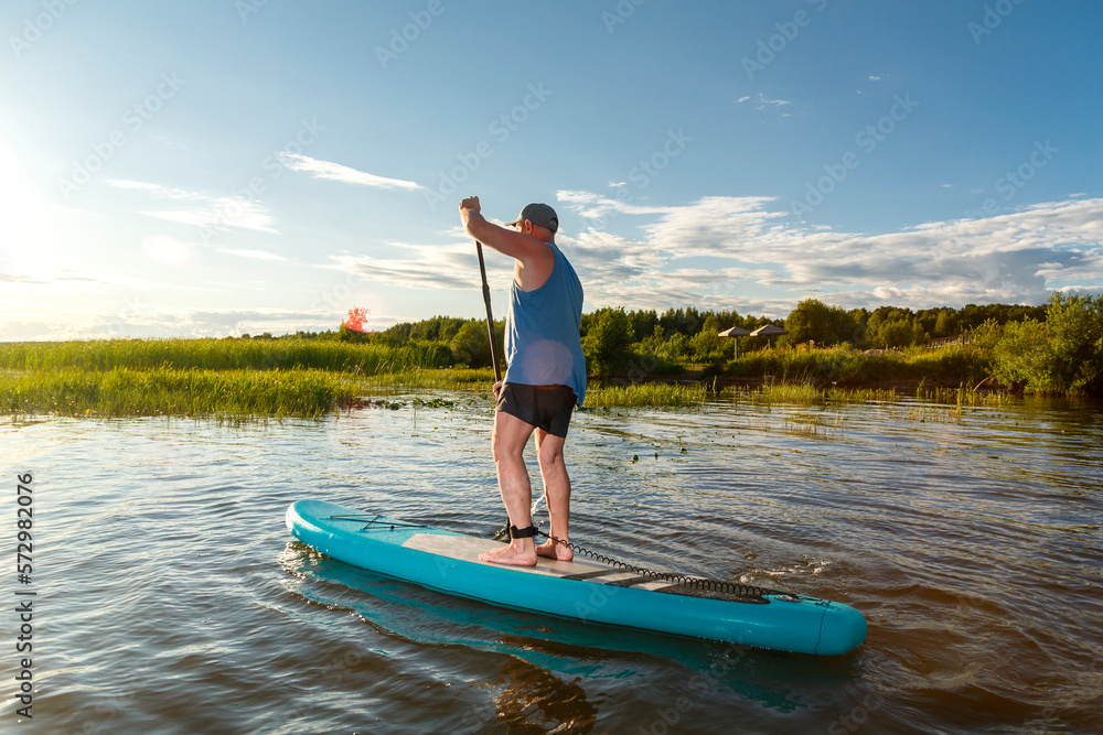 a man in shorts stands with a paddle on a sup board at sunset in the water.