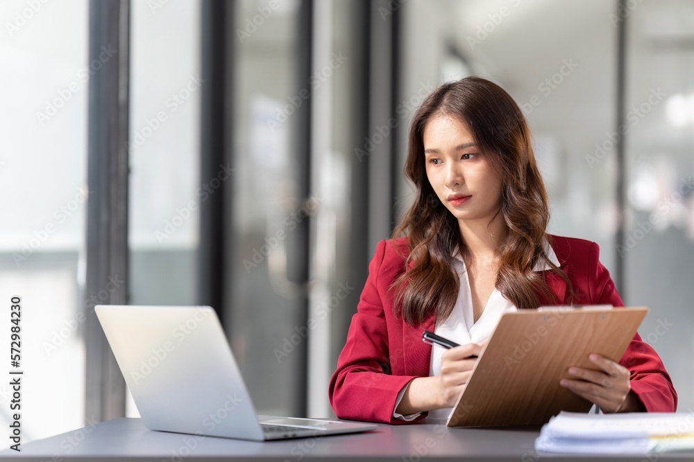 Young Asian businesswoman sitting at their desk and take notes using laptop in the office Young Asian businesswoman sitting at their desk and take notes using laptop in the office
