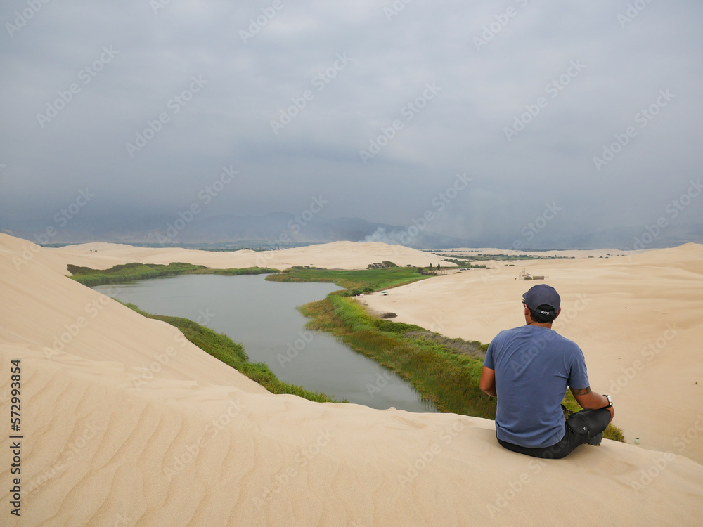 middle-aged man resting on a dune with sand barkhans next to Laguna Morón in the South American desert middle-aged man resting on a dune with sand barkhans next to Laguna Morón in the South American desert