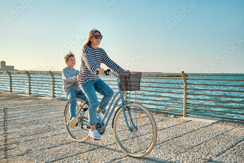 Fotografia Happy family, Carefree mother and son with bike riding on beach having fun, on the seaside promenade on a summer day, enjoying vacation