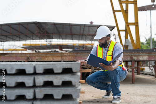Man engineer with document checking quality concrete panels floor. Foreman wearing vest and helmet safety working in factory produce precast concrete, construction industry