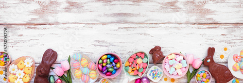 Easter candy bottom border. Top view over a white wood banner background. Chocolate bunnies, candy eggs and a selection of sweets. Copy space.