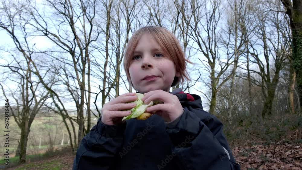 A young boy eats an outdoor sandwich. A boy of about nine years old is recuperating on a hike. A young boy eats an outdoor sandwich. A boy of about nine years old is recuperating on a hike.