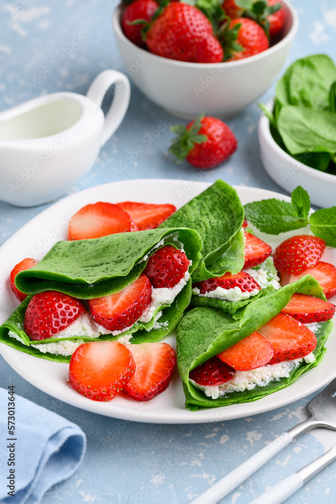 Spinach green crepes or pancakes with ricotta and strawberries on a plate for breakfast. Healthy spring or summer dessert. Selective focus
