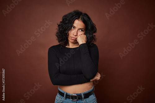 Young colombian curly hair woman isolated on brown background who feels sad and pensive, looking at copy space. © Asier