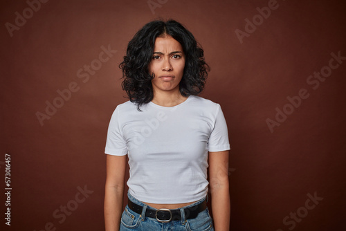 Young colombian curly hair woman isolated on brown background sad, serious face, feeling miserable and displeased.