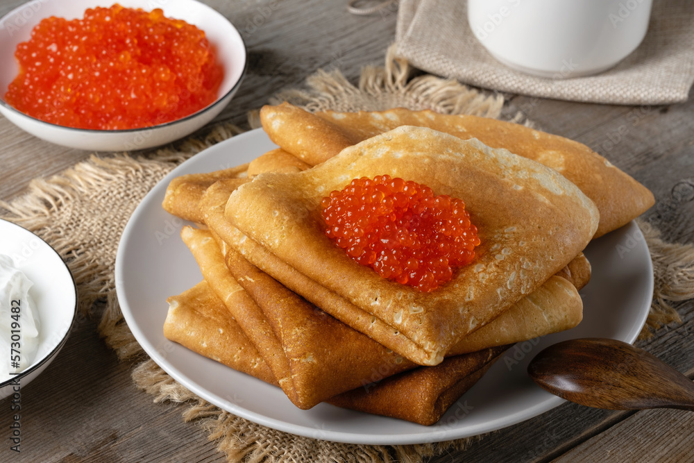 Stack of russian thin pancakes blini with red caviar on an old wooden table. Maslenitsa, traditional Russian blini