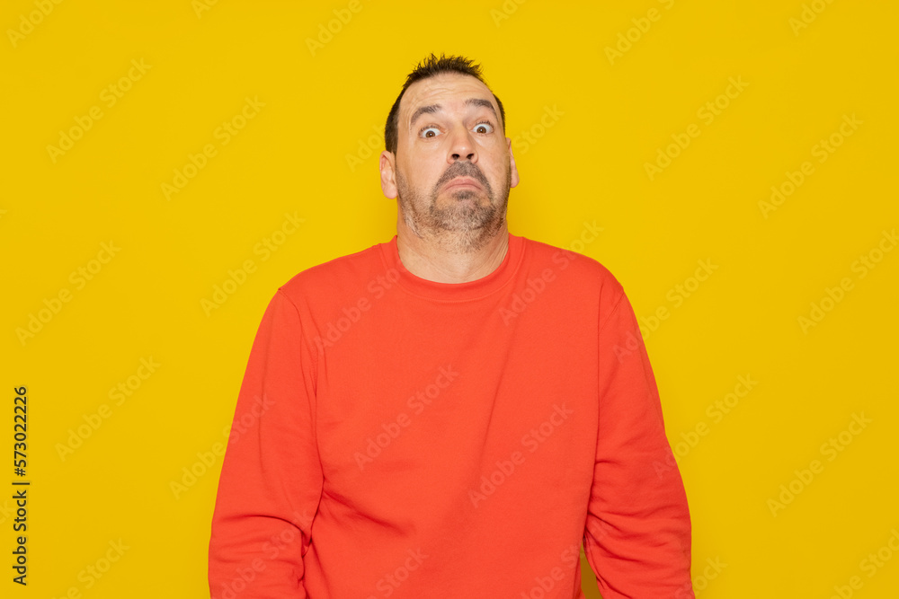 Obraz premium Bearded latino man wearing a red sweater with expression of doubt and confusion shrugging shoulders isolated over yellow background.