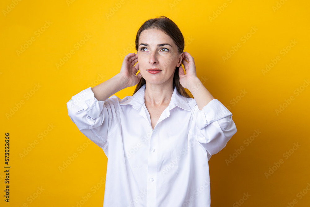 Smiling young woman in a white shirt straightens her hair on a yellow background Smiling young woman in a white shirt straightens her hair on a yellow background