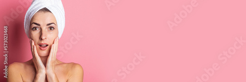 surprised young woman with towel on head, nude shoulders on pink background. Banner.