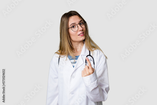 Compassionate female physician with a stethoscope around her neck  ready to diagnose and care for her patients in her signature white coat pointing with finger at you as if inviting come closer.